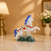 A decorative white horse figurine with blue, red, and gold details, standing on a green and white wave-like base on a polished marble surface in a warmly lit room.