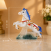 A decorative white horse figurine with blue mane and tail, red harness details, and a stone-textured base, shown on a tabletop with overlaid dimension lines and text indicating 24.5 cm length, 24 cm height, and 8 cm width.