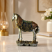 An ornate decorative horse figurine with a silver-toned body, detailed multicolor saddle and mane, and a rocky base, displayed on a marble surface in a softly lit interior setting.