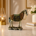 An ornate decorative horse figurine with a silver-toned body, gold saddle and bridle details, and a textured base, displayed on a light marble surface in a softly lit interior setting.