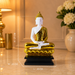 A seated Buddha statue with a glossy gold robe and a white face and hands, displayed on a black base in an indoor setting. White dotted measurement lines with labels showing height, width, and length are overlaid on the statue.