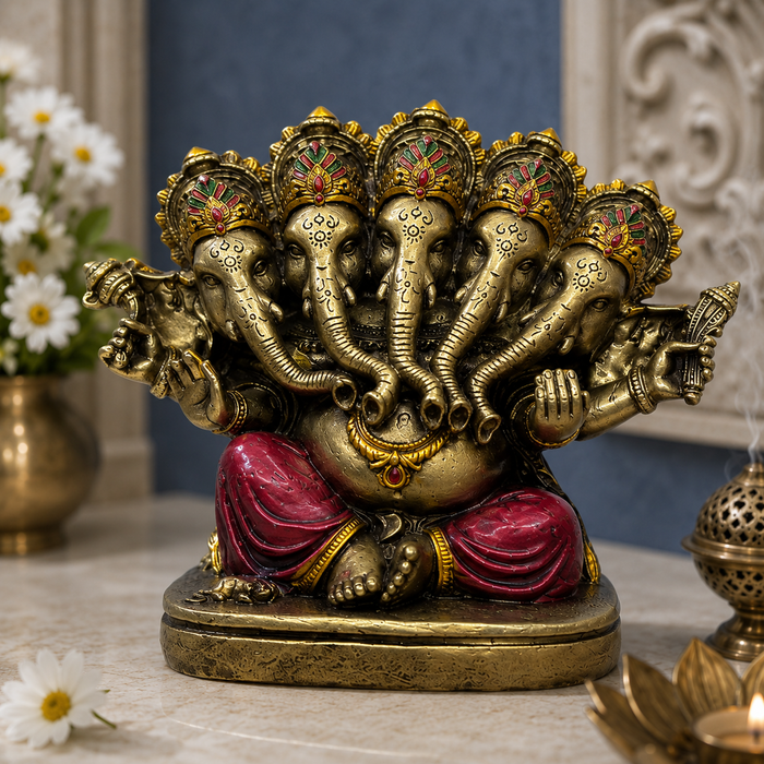 A multi-armed Lord Ganesha statue with a gold-toned finish, red draped pants, and colorful decorative headdresses, displayed on a marble surface with flowers and incense in the background.