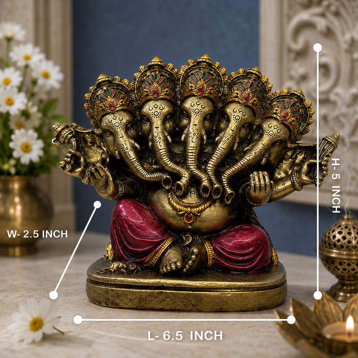 A brass-colored multi-armed Ganesha statue with red draped legs and gold accents, shown on a tabletop with white daisies in a vase and a lit lamp in the background. White measurement lines and text indicate dimensions: W-2.