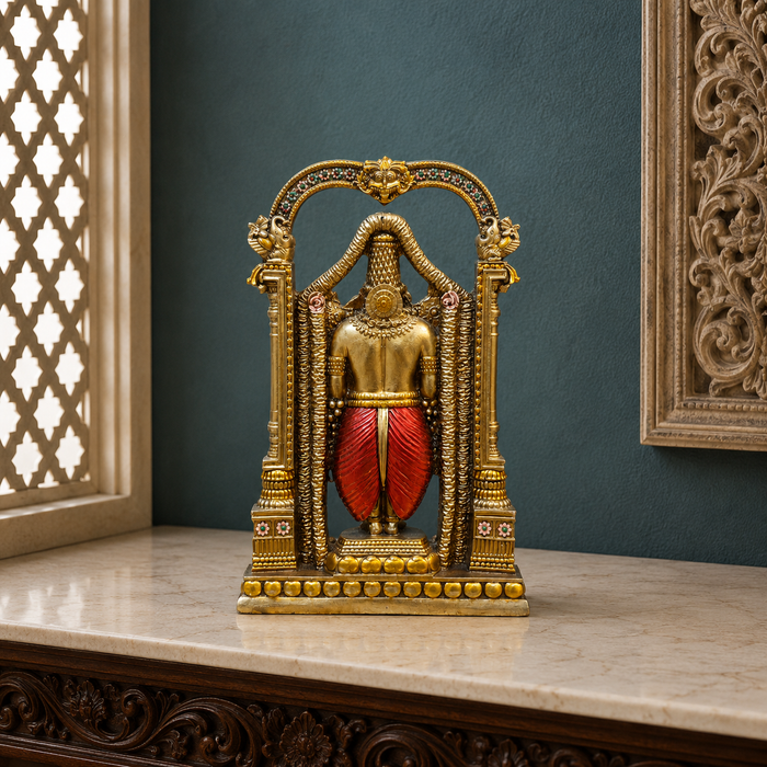An ornate gold-toned decorative statue of a seated figure framed within an arched structure, with a red draped lower garment, displayed on a marble surface against a dark teal wall.