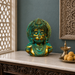 A decorative Lord Hanuman bust with a green patina finish, displayed on a marble-top console table in a styled interior setting.