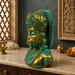 A decorative bust sculpture of a Hindu deity with a turquoise-green patina finish and gold accents, displayed on a marble countertop in a styled home decor setting.