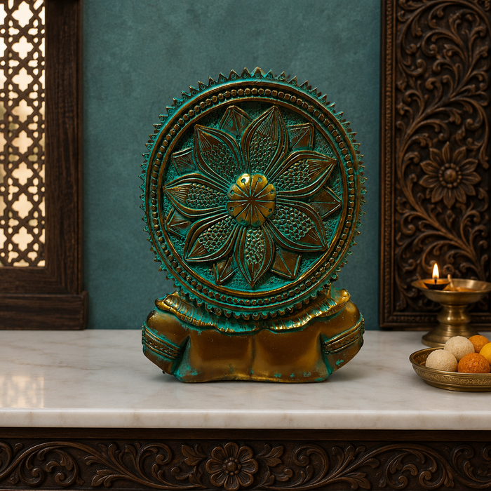A decorative circular wall plaque or sculpture with an ornate floral mandala design, featuring a turquoise and gold finish, displayed on a white marble surface in a styled interior setting.