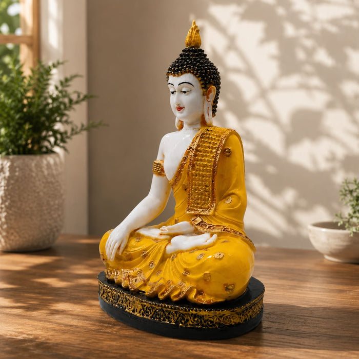 A golden Buddha statue seated in a meditative pose on a wooden table, with potted plants and soft leaf shadows in the background.