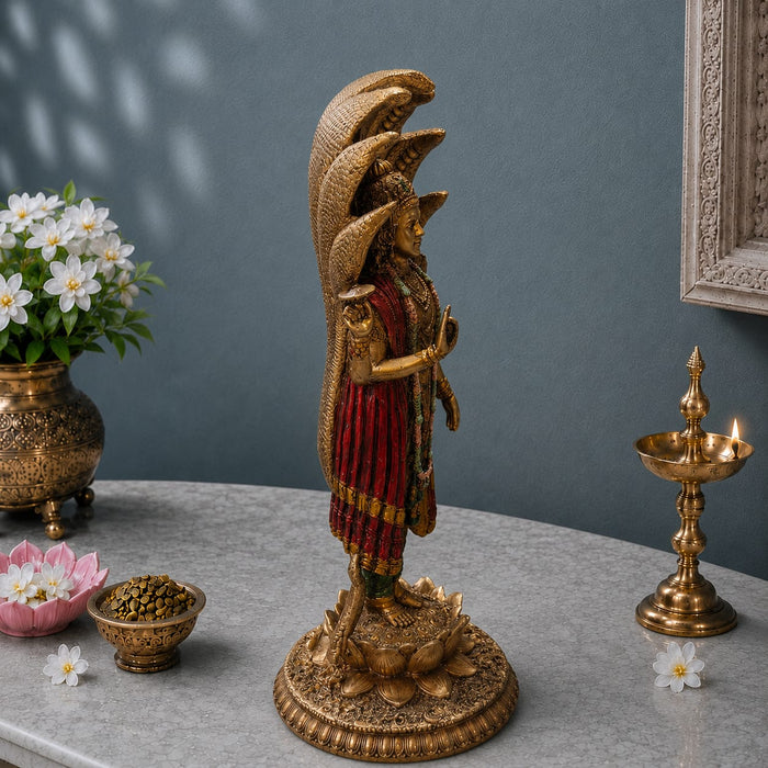 A golden statue of a multi-headed Hindu deity, likely Ganesha, standing on a lotus base, displayed on a gray marble tabletop with decorative props including a brass lamp, flowers, and a vase.