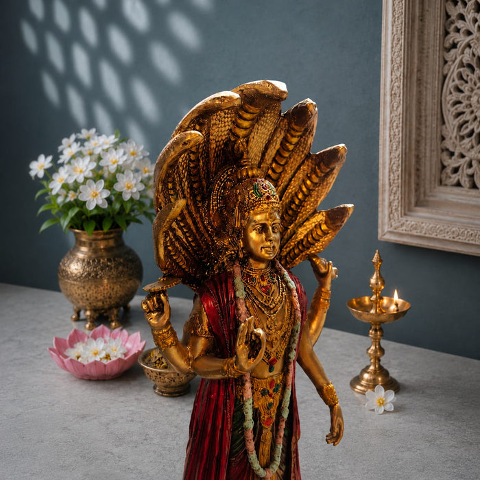 A golden Lord Shiva statue with a multi-headed snake canopy, standing on a gray stone surface next to a brass diya, a pink lotus bowl, and a vase of white flowers against a dark blue-gray wall.