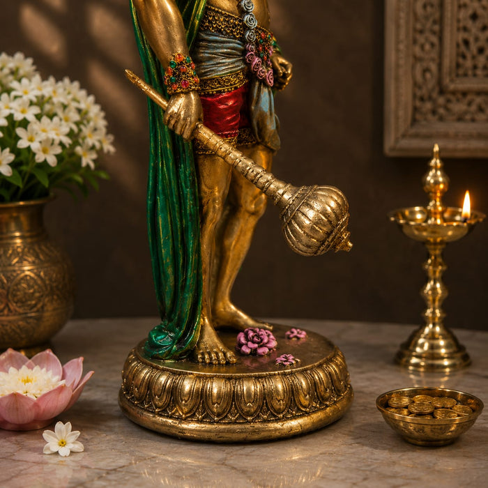 A decorative golden statue of a Hindu deity standing on a lotus base, styled on a tabletop with flowers, a lit brass diya, and a small bowl in a warm indoor setting.