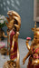A close-up of a decorative golden Hindu deity statue, likely Shiva Nataraja, with a multi-headed snake canopy and red draped garments, shown alongside another similar statue in an indoor setting.