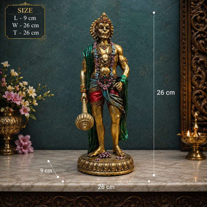 Gold-toned Hindu deity statue holding a mace, displayed on a marble surface with overlaid size measurements (26 cm by 26 cm by 9 cm) against a dark teal wall with decorative flowers and a brass lamp.